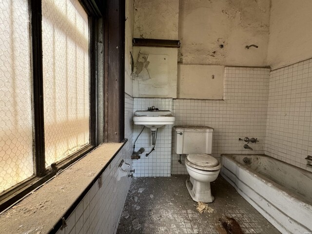 bathroom featuring a tub, a sink, tile walls, and toilet