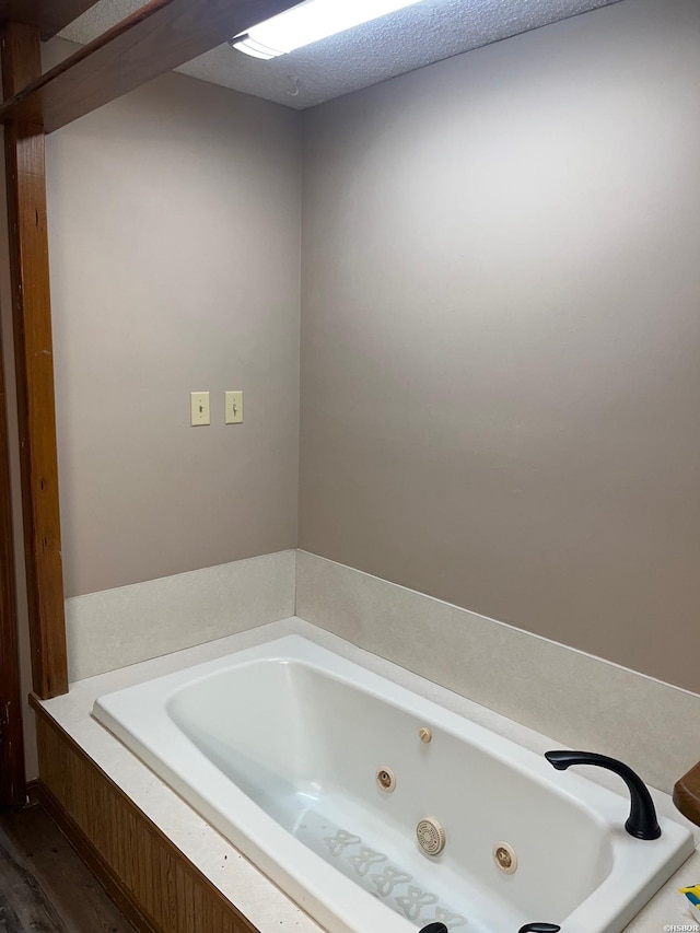 bathroom with a textured ceiling, a tub with jets, and wood finished floors