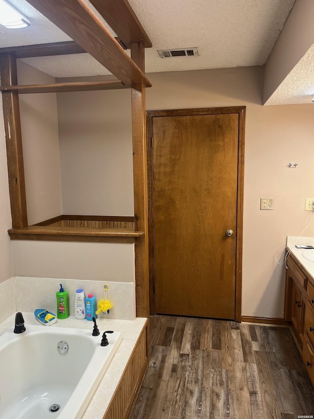 full bath with visible vents, wood finished floors, a textured ceiling, vanity, and a bath