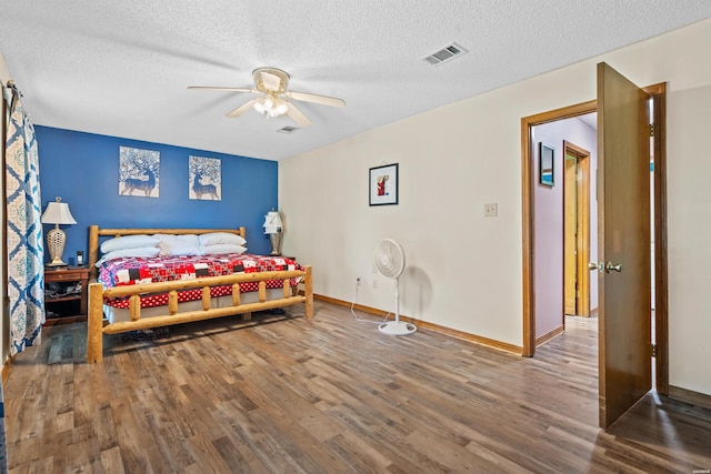 bedroom with a textured ceiling, ceiling fan, wood finished floors, visible vents, and baseboards