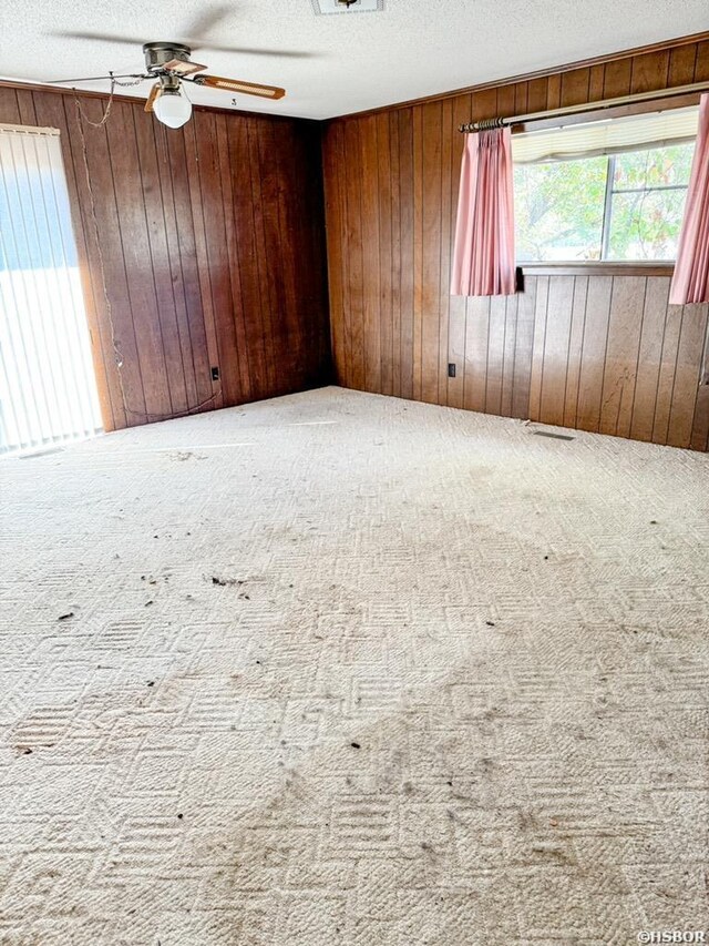 carpeted spare room featuring ceiling fan, wooden walls, visible vents, and a textured ceiling