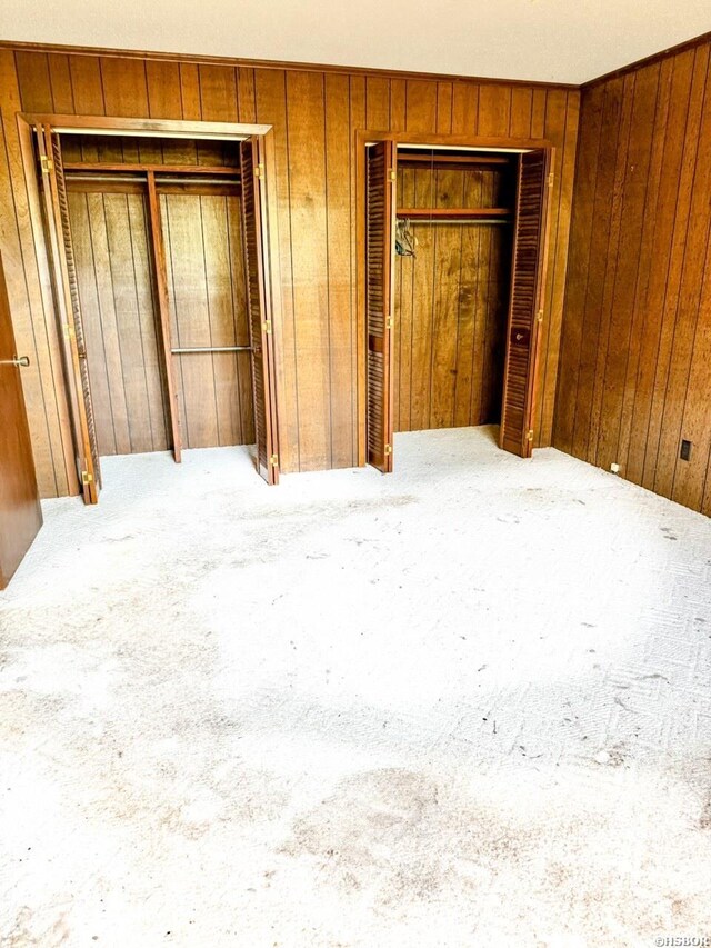 unfurnished bedroom with carpet floors, wood walls, and multiple closets