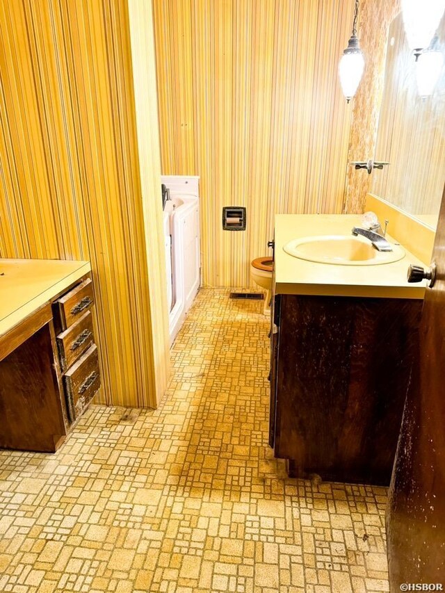 full bathroom featuring toilet, brick floor, and vanity