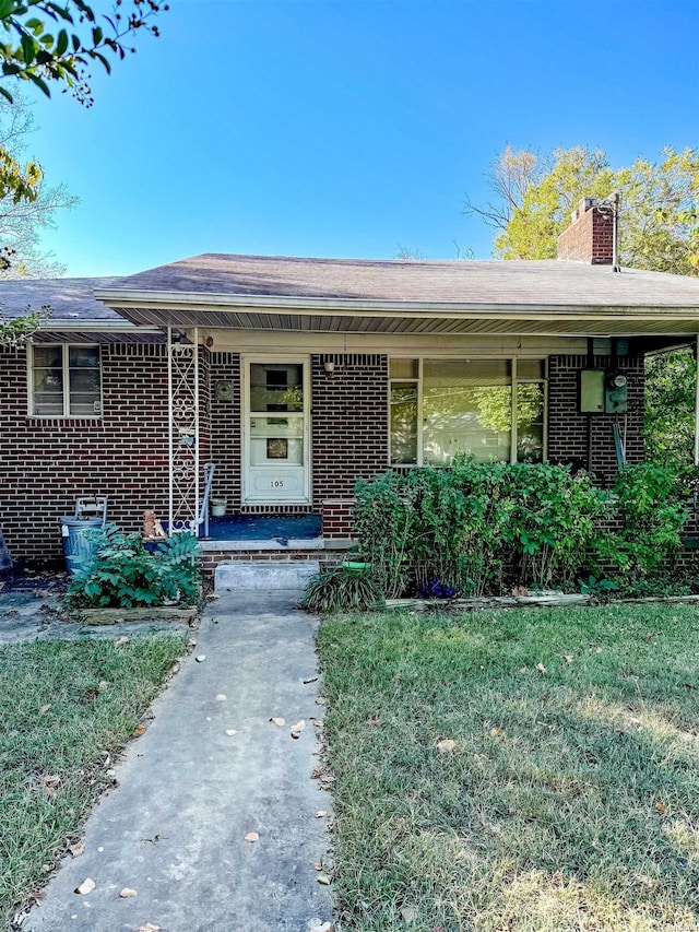 doorway to property with a yard, a chimney, and brick siding