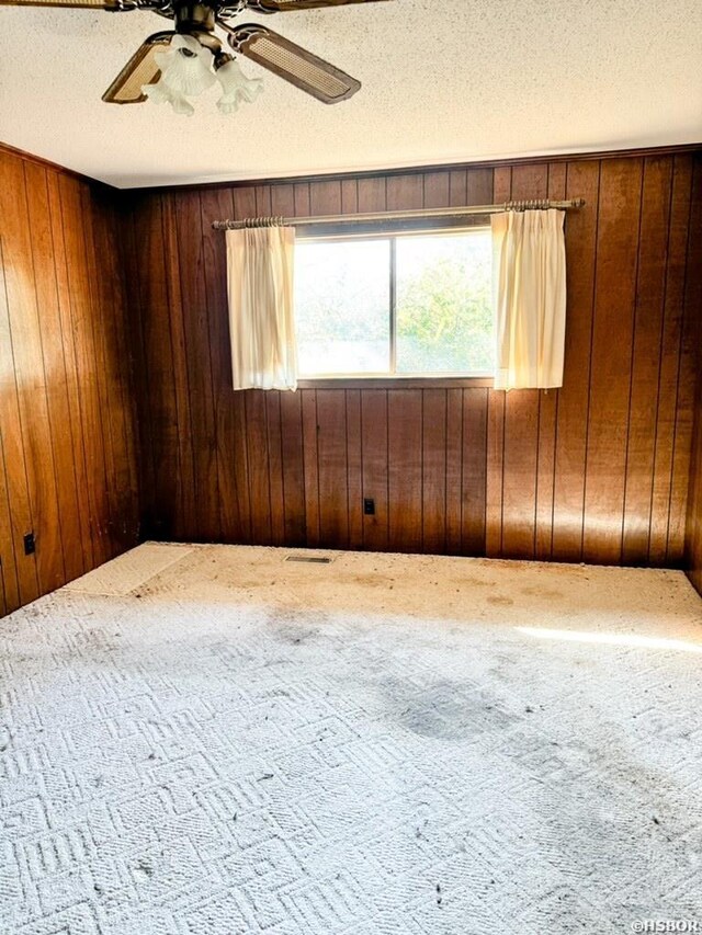 carpeted spare room featuring a textured ceiling, a ceiling fan, and wooden walls