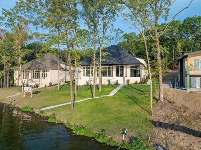 rear view of house featuring a lawn, a water view, and stucco siding