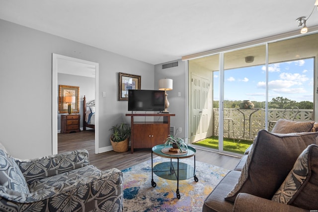 living area with a wall of windows, wood finished floors, visible vents, and baseboards