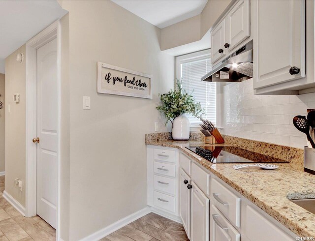 kitchen with white cabinets, light stone counters, black electric cooktop, under cabinet range hood, and backsplash