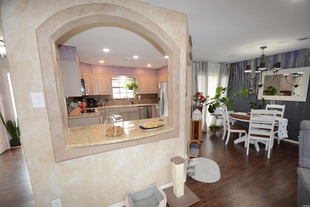 kitchen featuring arched walkways, dark wood-style flooring, stainless steel appliances, light brown cabinetry, and a sink