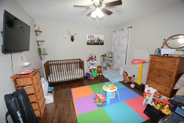 bedroom featuring visible vents, a crib, dark wood-style flooring, and a ceiling fan