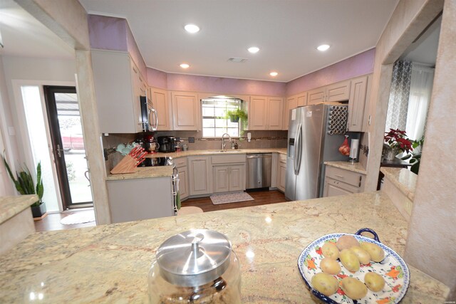 kitchen with light stone counters, stainless steel appliances, tasteful backsplash, visible vents, and a sink