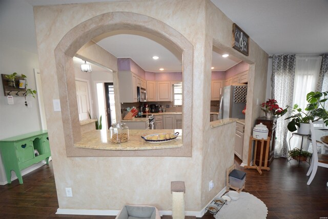 kitchen with arched walkways, light brown cabinetry, appliances with stainless steel finishes, and dark wood-style floors