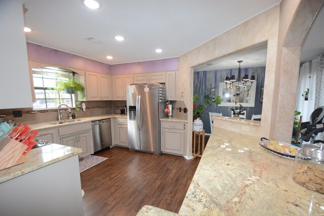 kitchen with a peninsula, a sink, hanging light fixtures, appliances with stainless steel finishes, and dark wood-style floors