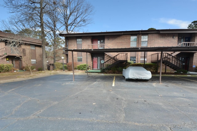 view of building exterior featuring covered and uncovered parking and stairs