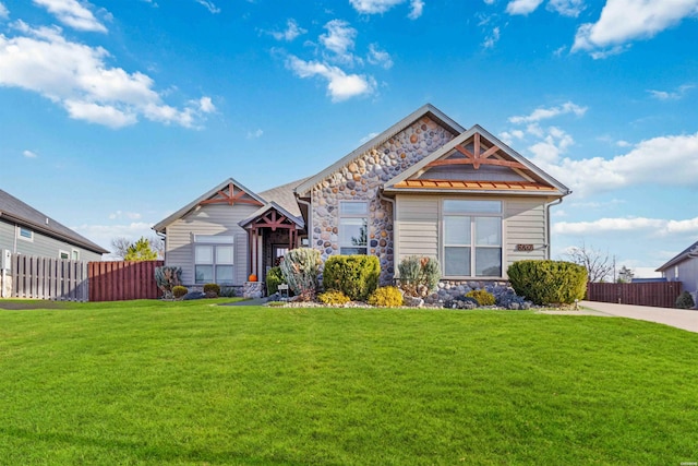 craftsman-style home with stone siding, a front yard, and fence