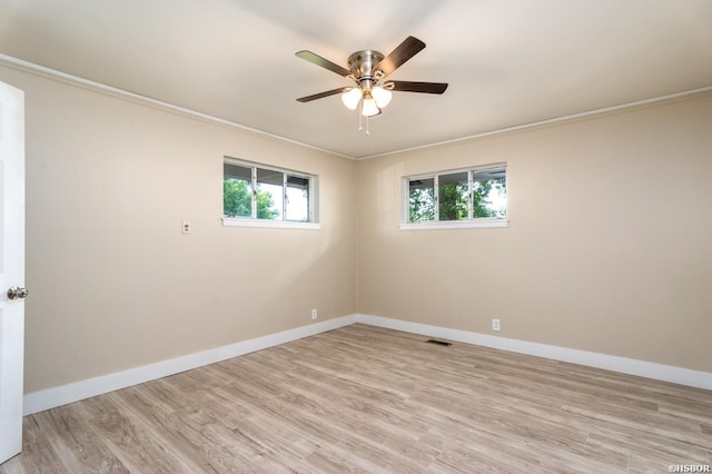 empty room with light wood-style flooring, visible vents, baseboards, and ornamental molding