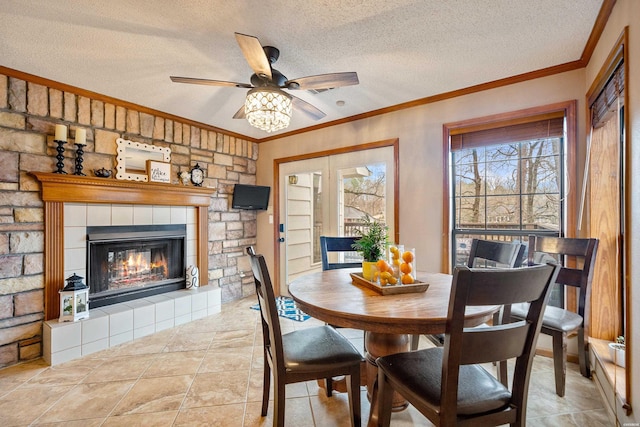 dining room with crown molding, a textured ceiling, a tiled fireplace, and ceiling fan