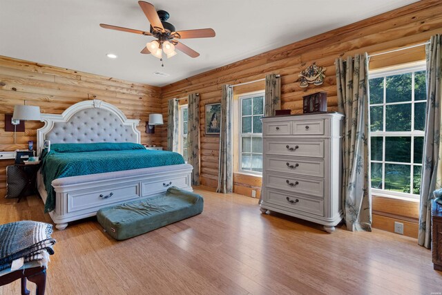 bedroom featuring light wood finished floors, multiple windows, log walls, and a ceiling fan