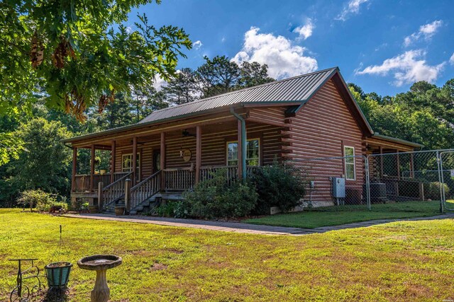 cabin with covered porch, metal roof, log exterior, fence, and a front lawn