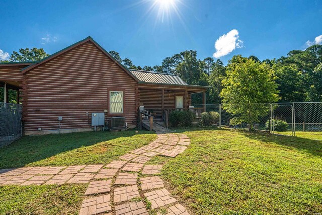 back of property with a lawn, central AC unit, metal roof, fence, and log siding