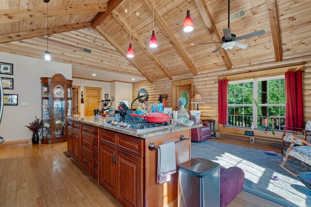 kitchen featuring high vaulted ceiling, light stone counters, a kitchen island, stainless steel gas stovetop, and pendant lighting