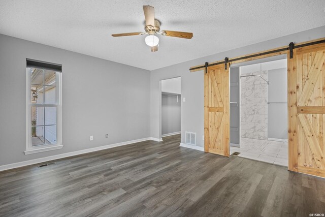 unfurnished bedroom with dark wood-type flooring, visible vents, a textured ceiling, and a barn door