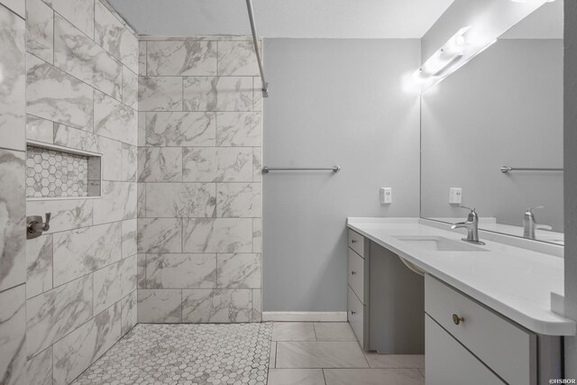 bathroom with marble finish floor, a tile shower, vanity, and baseboards