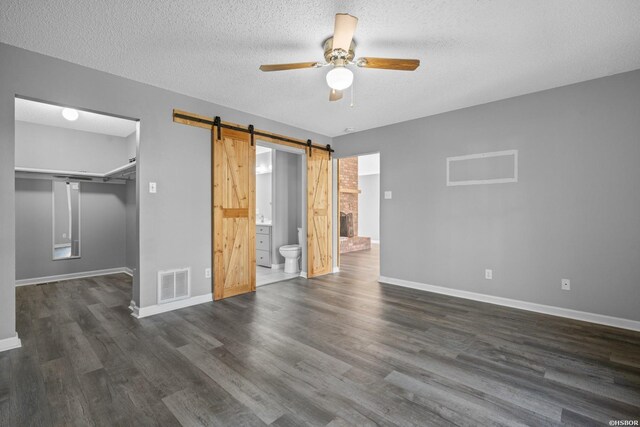 unfurnished bedroom with dark wood-style floors, a walk in closet, visible vents, a barn door, and baseboards