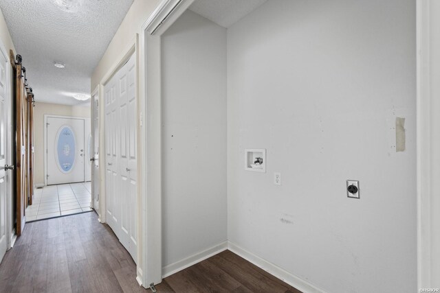 hall featuring light wood-type flooring, a barn door, baseboards, and a textured ceiling