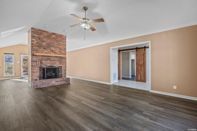 unfurnished living room with a barn door, a fireplace, visible vents, vaulted ceiling, and dark wood-style floors