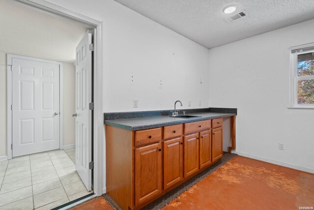 kitchen with visible vents, brown cabinetry, dark countertops, a textured ceiling, and a sink