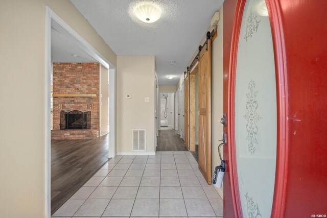 hallway with light tile patterned floors, visible vents, a textured ceiling, and a barn door