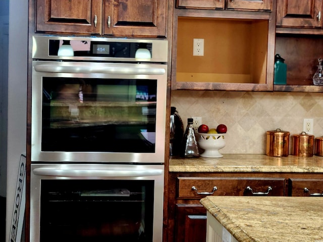 kitchen with light stone counters, stainless steel double oven, and backsplash