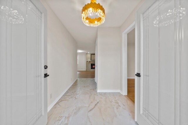 corridor with marble finish floor, baseboards, and a notable chandelier