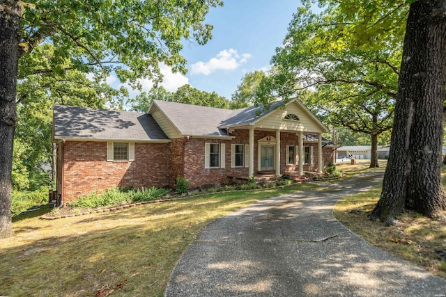 view of front of home with driveway, brick siding, roof with shingles, a porch, and a front yard