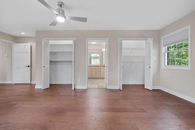 unfurnished bedroom featuring baseboards, wood finished floors, and multiple closets