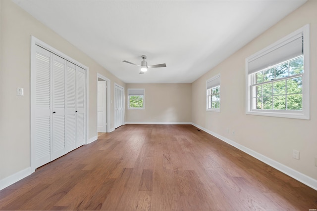 unfurnished bedroom with baseboards, wood finished floors, a ceiling fan, and multiple closets