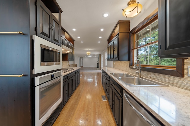 kitchen featuring under cabinet range hood, a sink, appliances with stainless steel finishes, light wood finished floors, and tasteful backsplash