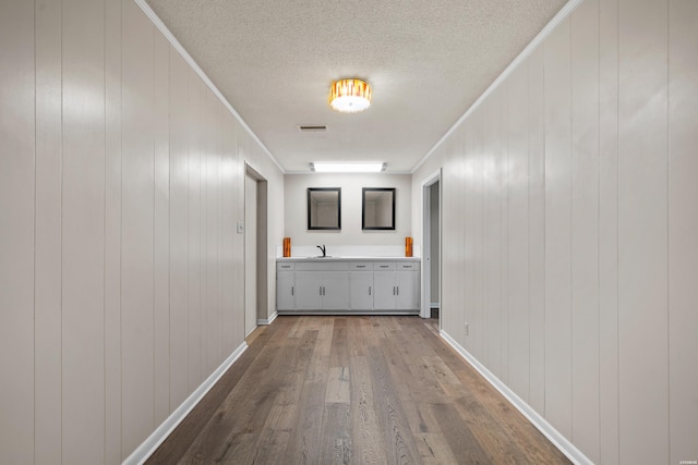 corridor with a textured ceiling, wood finished floors, a sink, baseboards, and crown molding