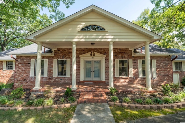 view of front facade featuring french doors, a porch, roof with shingles, and brick siding