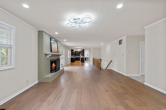 unfurnished living room with ornamental molding, light wood finished floors, a brick fireplace, and visible vents