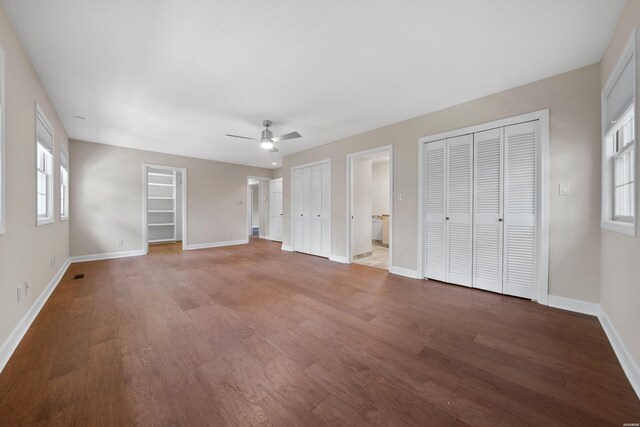 unfurnished bedroom featuring baseboards, multiple closets, and wood finished floors