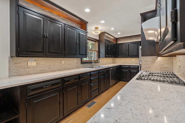 kitchen featuring stainless steel appliances, tasteful backsplash, light wood-style flooring, a sink, and light stone countertops