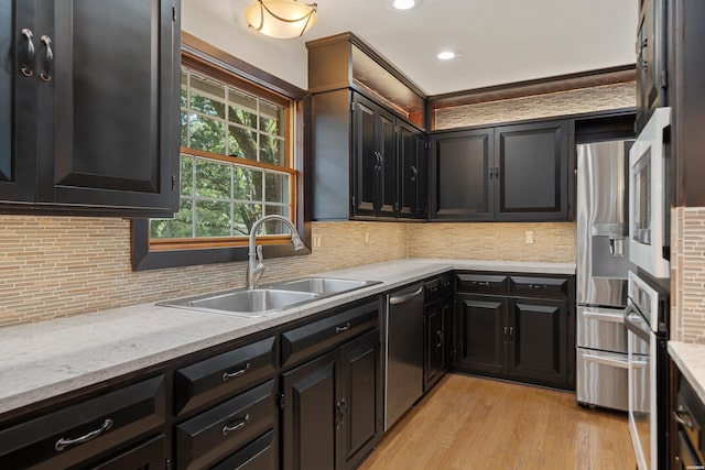 kitchen featuring light stone counters, light wood-style flooring, a sink, appliances with stainless steel finishes, and backsplash