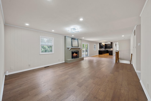 unfurnished living room with recessed lighting, a brick fireplace, crown molding, and wood finished floors