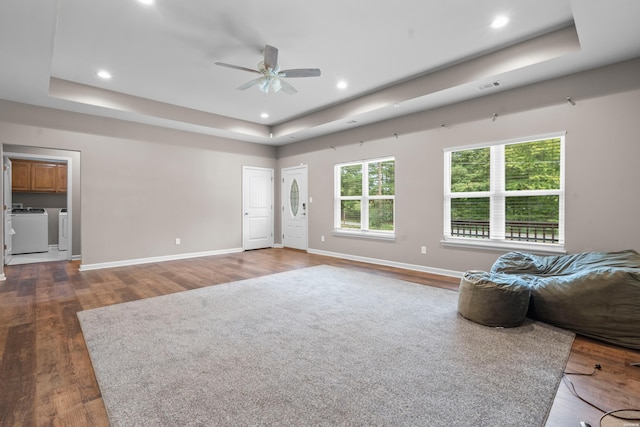 unfurnished living room with baseboards, a raised ceiling, wood finished floors, and washing machine and clothes dryer