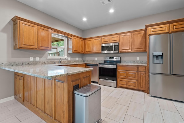 kitchen with light stone counters, stainless steel appliances, visible vents, brown cabinetry, and a peninsula