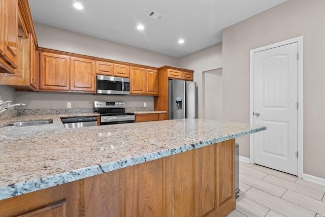 kitchen featuring visible vents, brown cabinets, light stone countertops, stainless steel appliances, and a sink