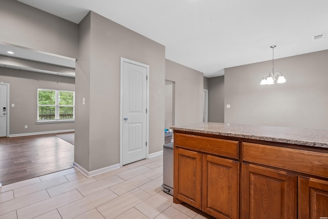 kitchen with visible vents, brown cabinetry, light stone counters, hanging light fixtures, and a notable chandelier