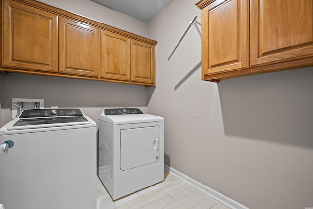 clothes washing area with washing machine and dryer, cabinet space, and baseboards